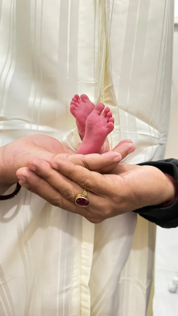 Neonatal intensive care unit with nurses in blue gowns and masks tending to newborns in incubators.