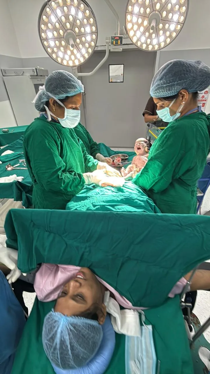 Newborn in a neonatal incubator being cared for by a nurse in blue scrubs in a NICU, with monitors and equipment nearby into the scene.